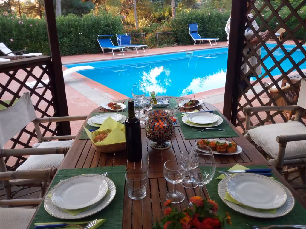 Outdoor dining setup by a pool with traditional Italian dishes, part of the Alghero cooking class experience in Olmedo.