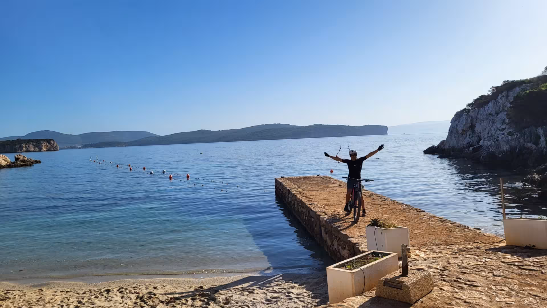 Smiling biker gives thumbs up amidst lush greenery and coastal views in Porto Conte Park, Alghero.