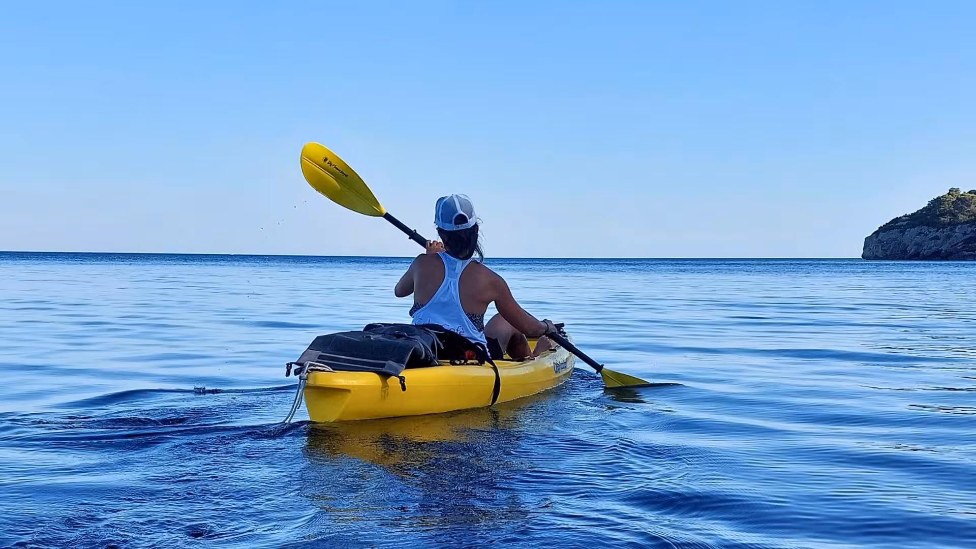 Solo kayaker paddling on the serene waters of Porto Conte Park in Alghero, enjoying a peaceful kayaking tour.