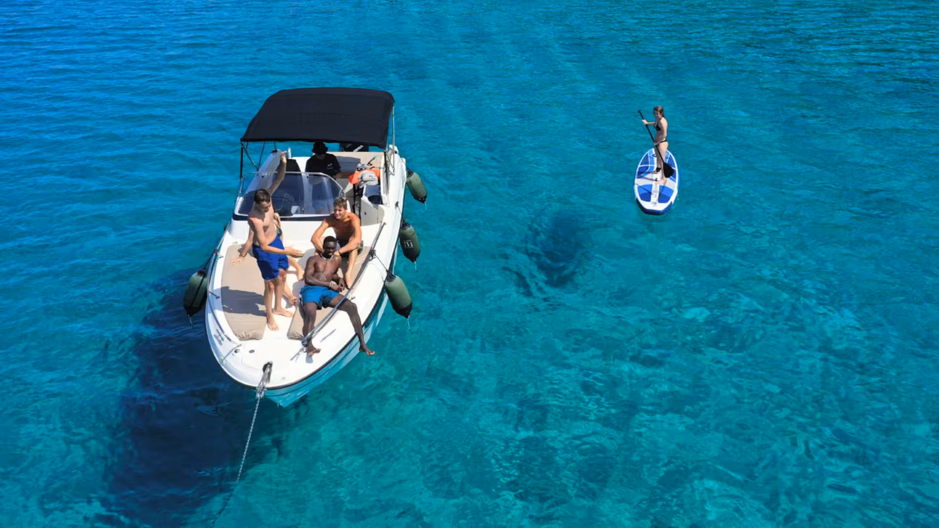 Group enjoying a motor boat ride and paddleboarding on clear waters during a half-day tour from Alghero.