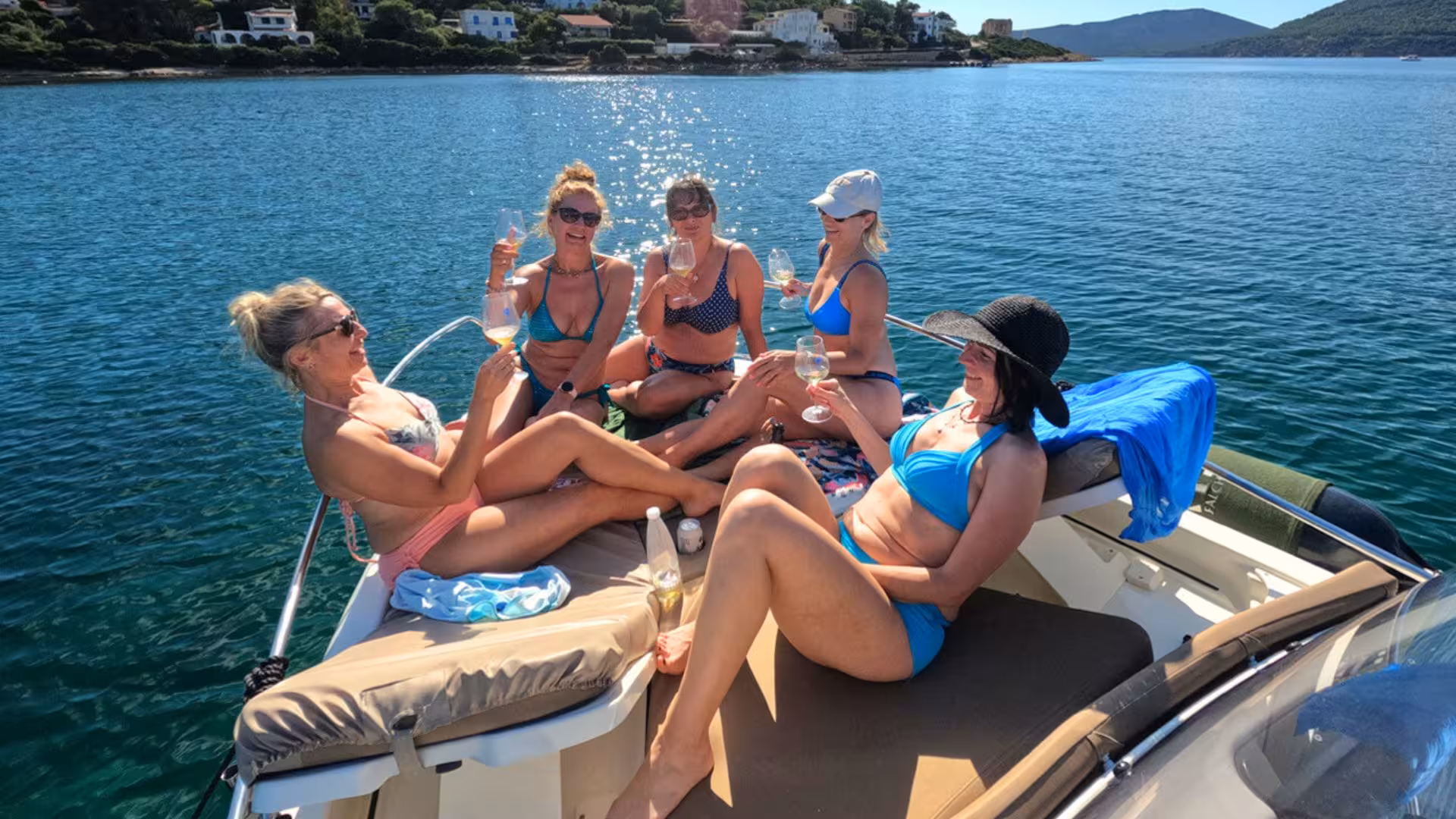 Group of friends toasting with drinks on a motor boat, enjoying a sunny day near Alghero's coastline.