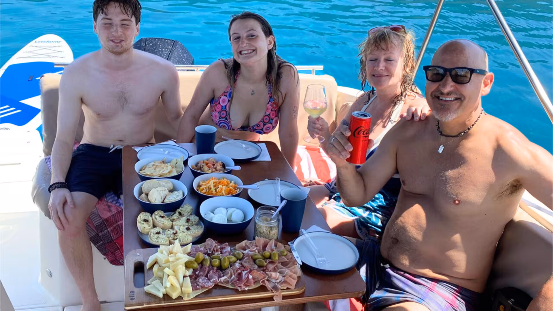 Guests enjoying a delicious spread of local delicacies on a motor boat trip from Alghero, surrounded by turquoise waters.