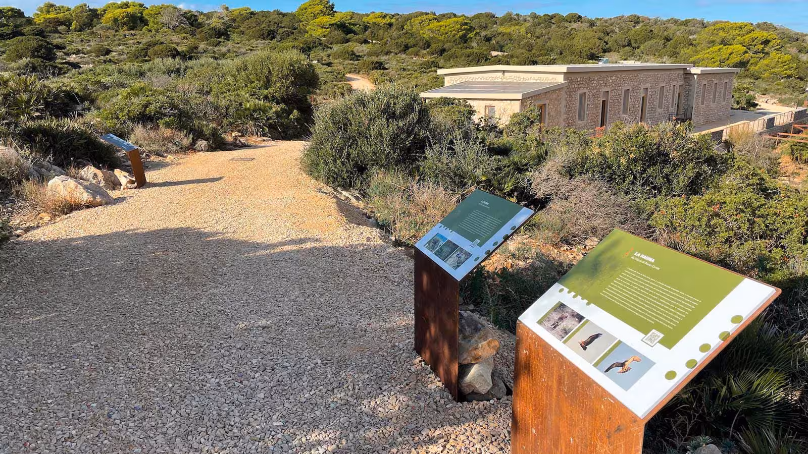 Explore Porto Conte Park Ecomuseum's scenic trails with informative signs amidst lush greenery in Alghero.