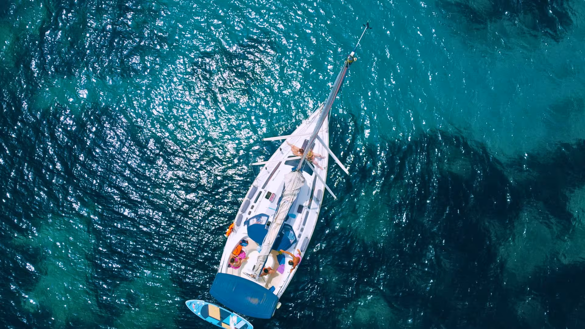 Aerial view of a sailboat cruising through the sparkling turquoise waters of Porto Conte Park near Alghero.