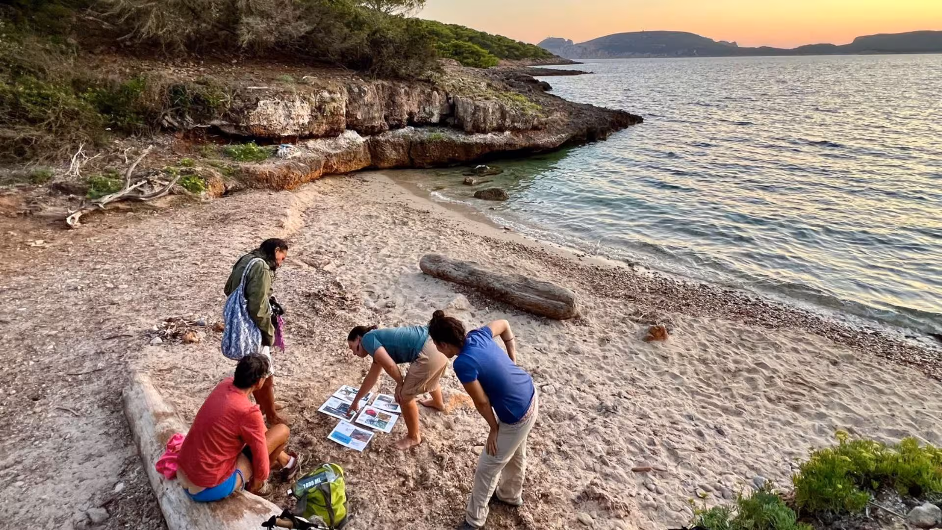 Tourists examining maps on a serene sandy beach at sunset in Porto Conte, Alghero, perfect for trekking tours.