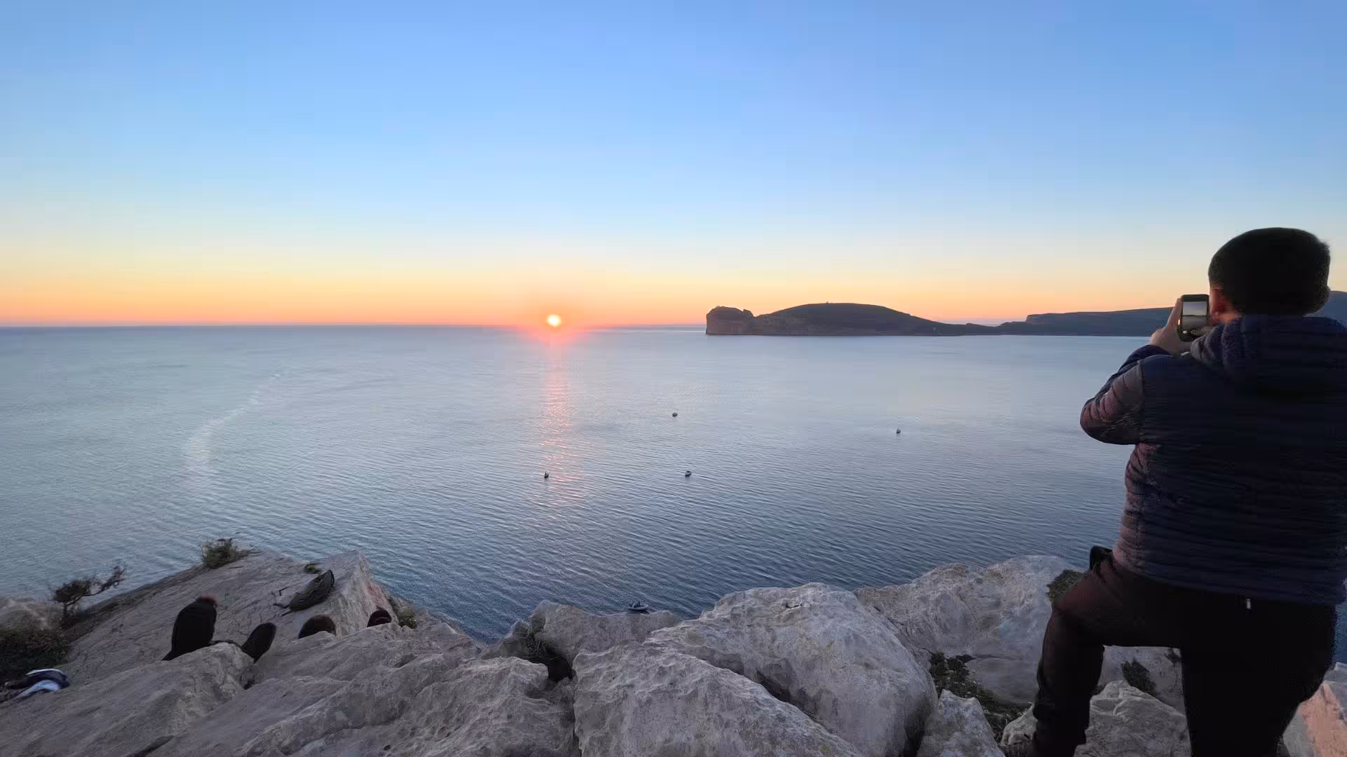 Hiker capturing a stunning sunset over the sea from the cliffs of Porto Conte Park in Alghero, perfect for trekking.