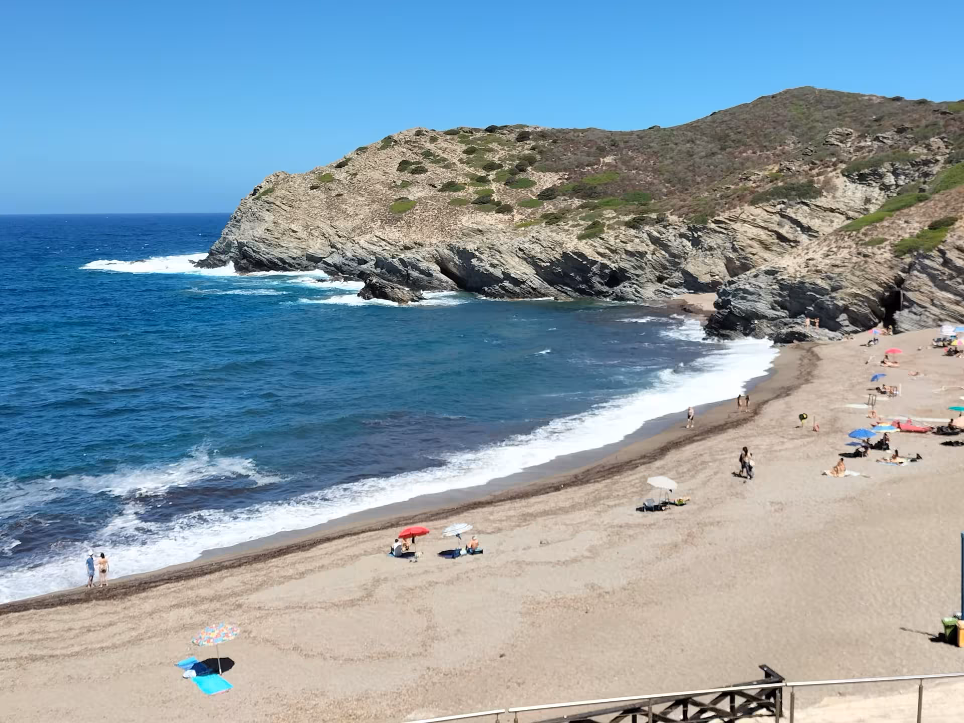 Serene Porto Ferro beach with sunbathers and umbrellas, a scenic spot on the Alghero off-road tour to Sardinia's coastline.