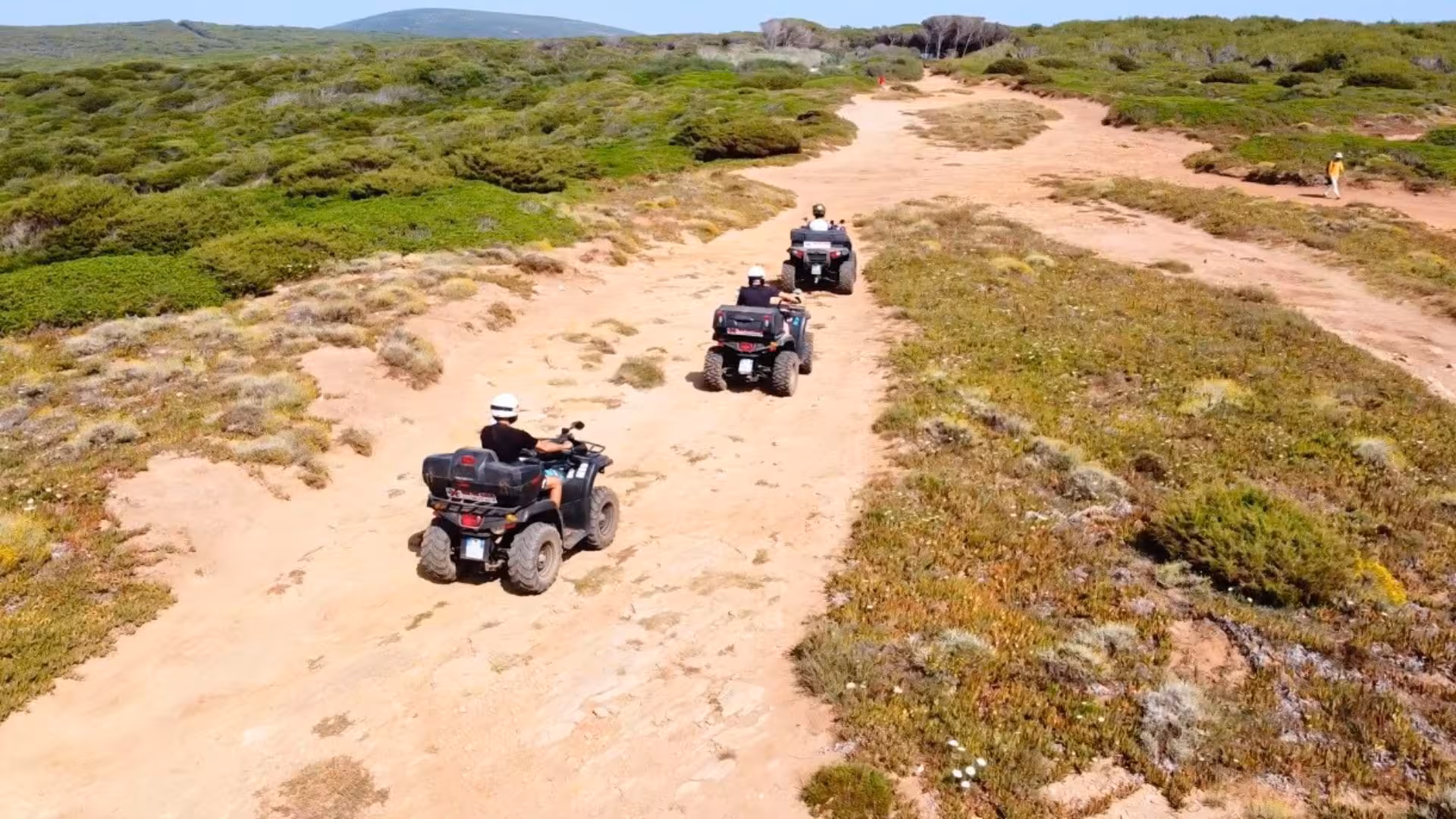 Group of riders exploring Alghero's scenic trails on a quad tour, surrounded by lush greenery and open landscapes.