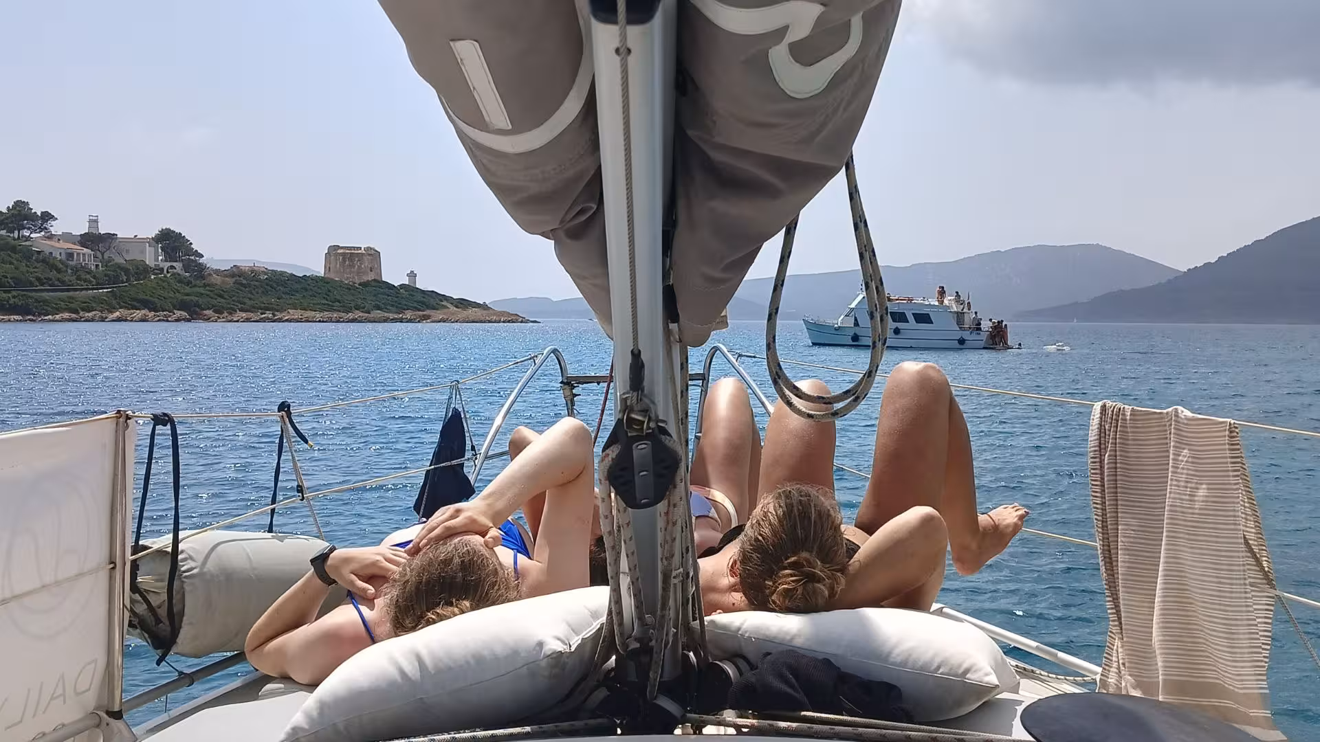 Relaxing on a sailboat deck with stunning coastal views during an Alghero sailing boat tour.