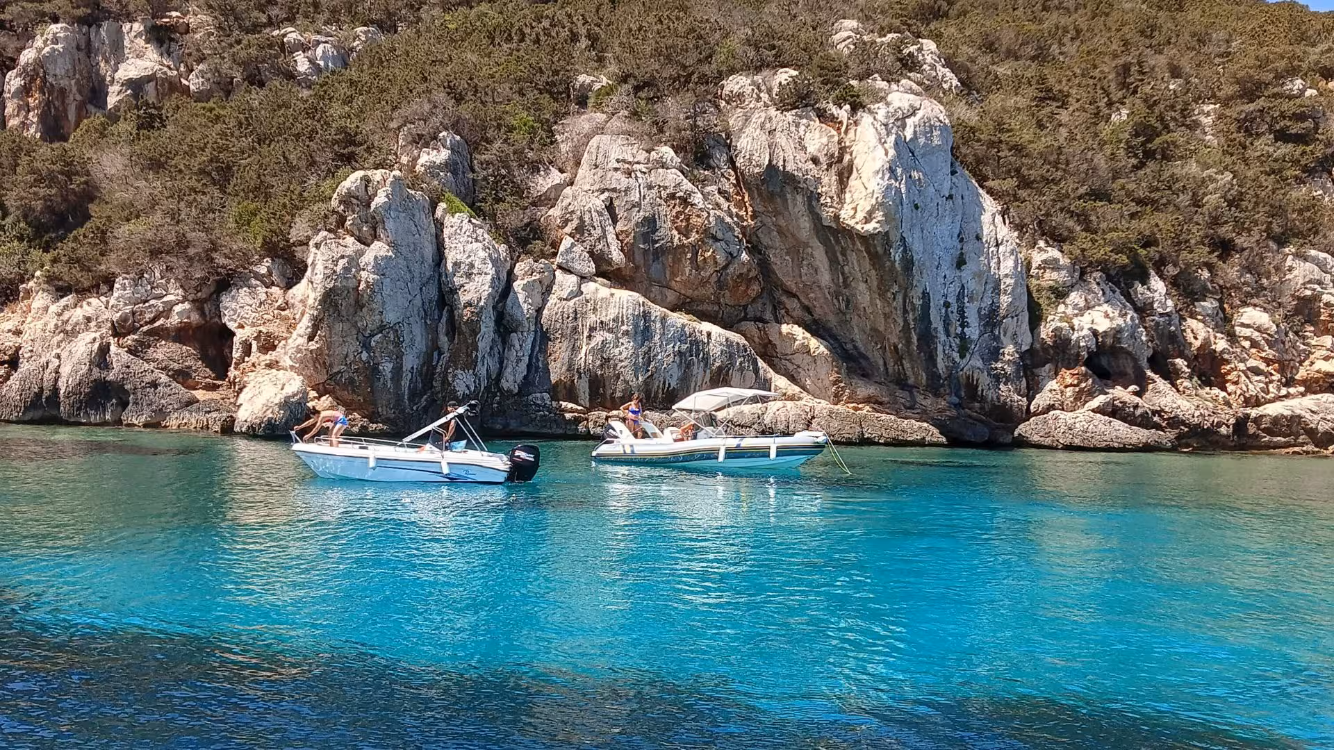 Two boats anchored near rocky cliffs and turquoise waters on a scenic Alghero sailing excursion.