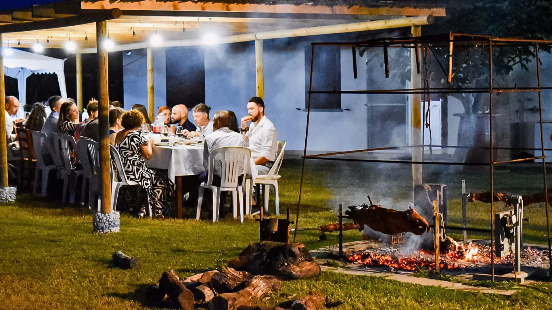 Guests savoring a traditional Sardinian meal in Alghero vineyard with a rustic outdoor grill setting.