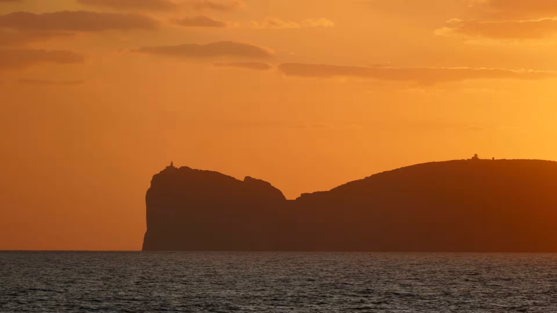 Stunning sunset view over Porto Conte Park cliffs during Alghero catamaran tour.