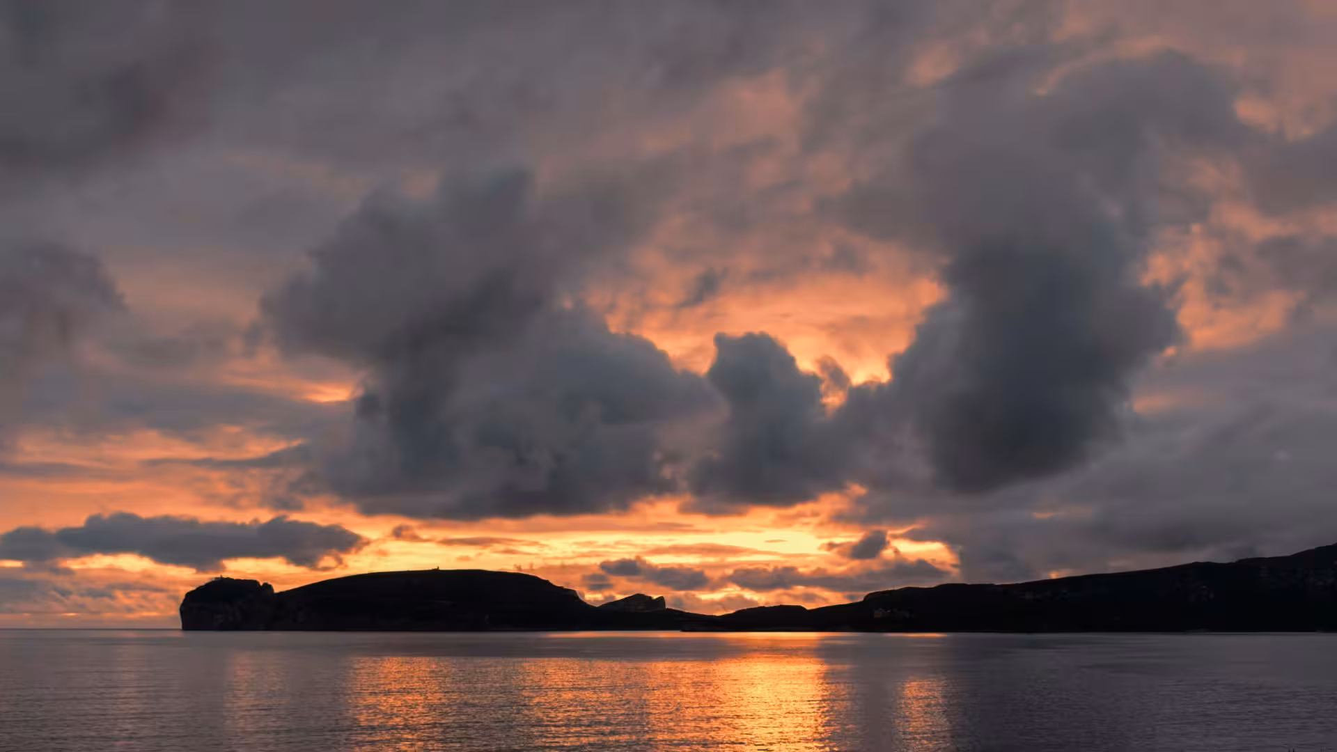 Dramatic Alghero sunset with vibrant orange hues and silhouetted cliffs over tranquil sea during private dinghy tour.