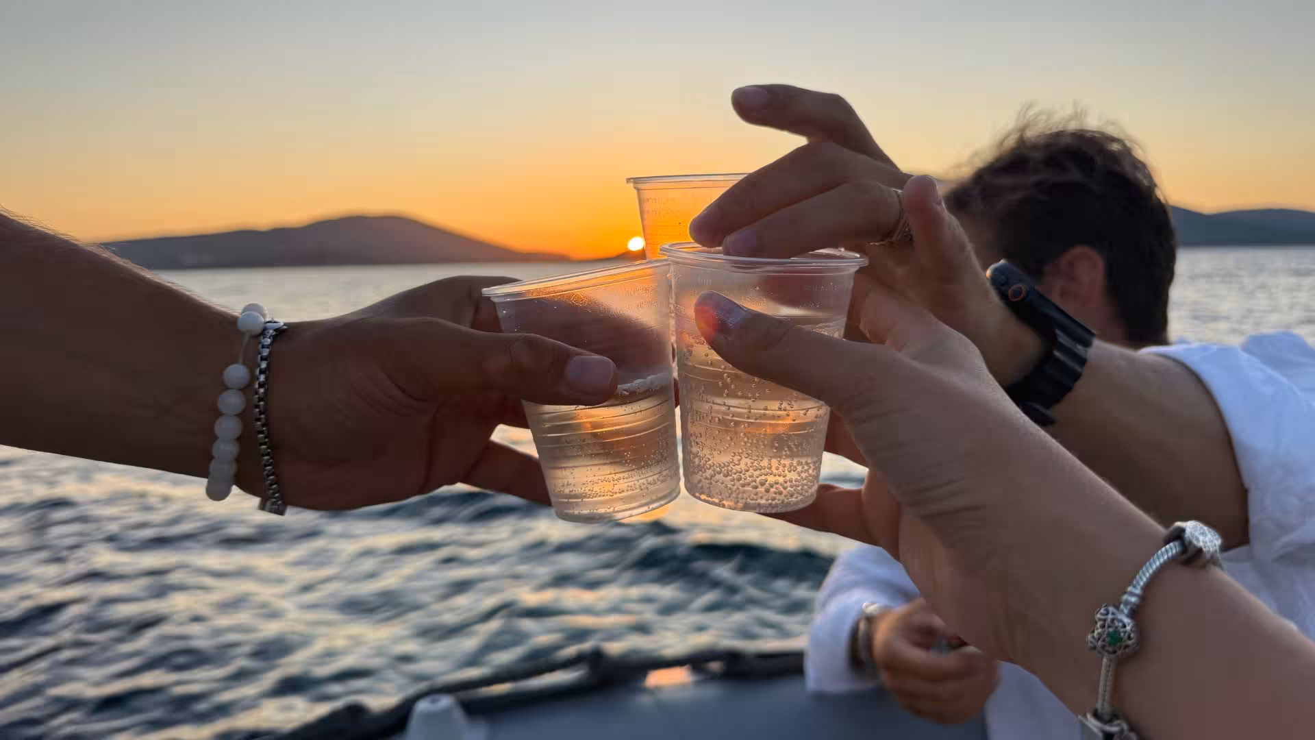 Toasting with drinks at sunset on an Alghero dinghy tour, celebrating a memorable evening on the Sardinian waters.