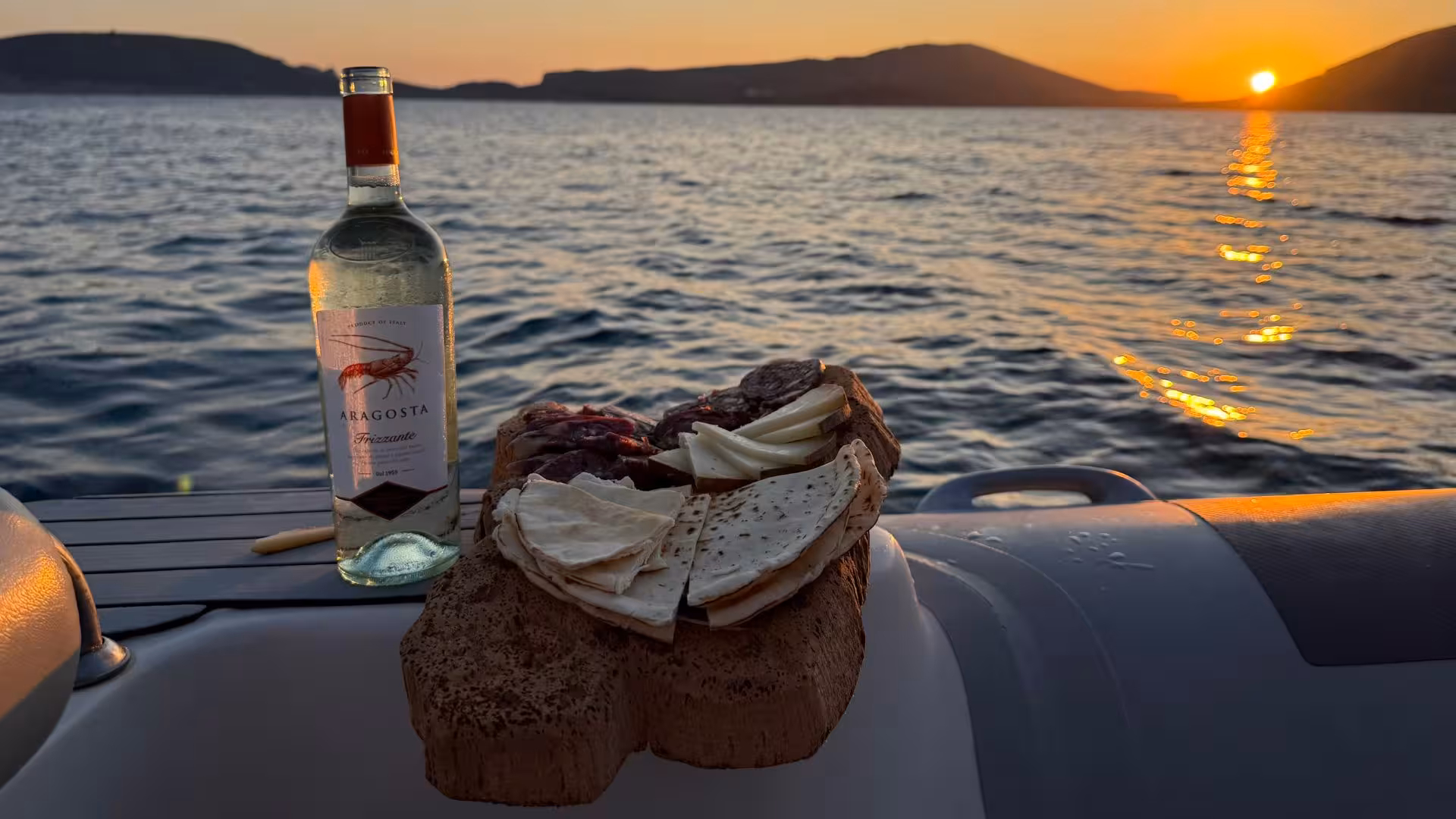 Wine and cheese on a dinghy at sunset in Alghero, showcasing a perfect culinary experience on the Mediterranean Sea.
