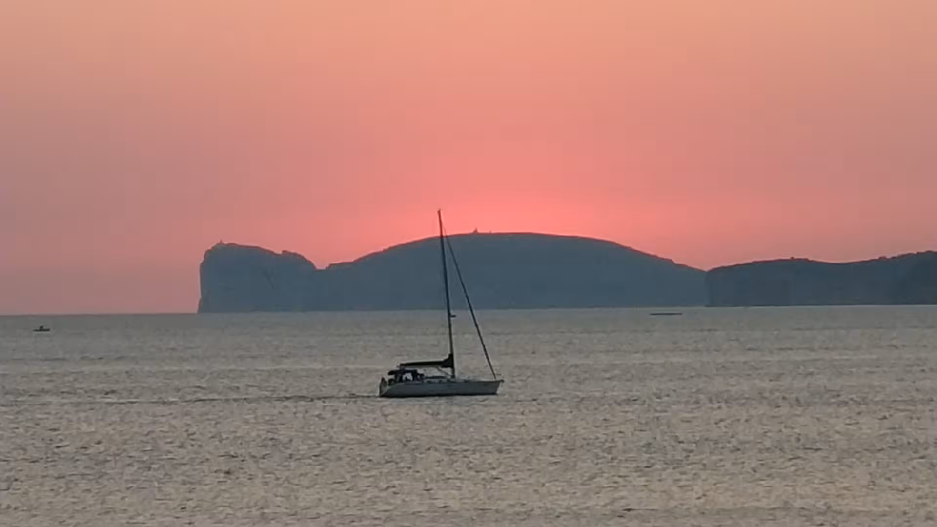 Sailboat gliding on the sea with a pink sunset backdrop near Alghero, offering a serene sailing adventure.