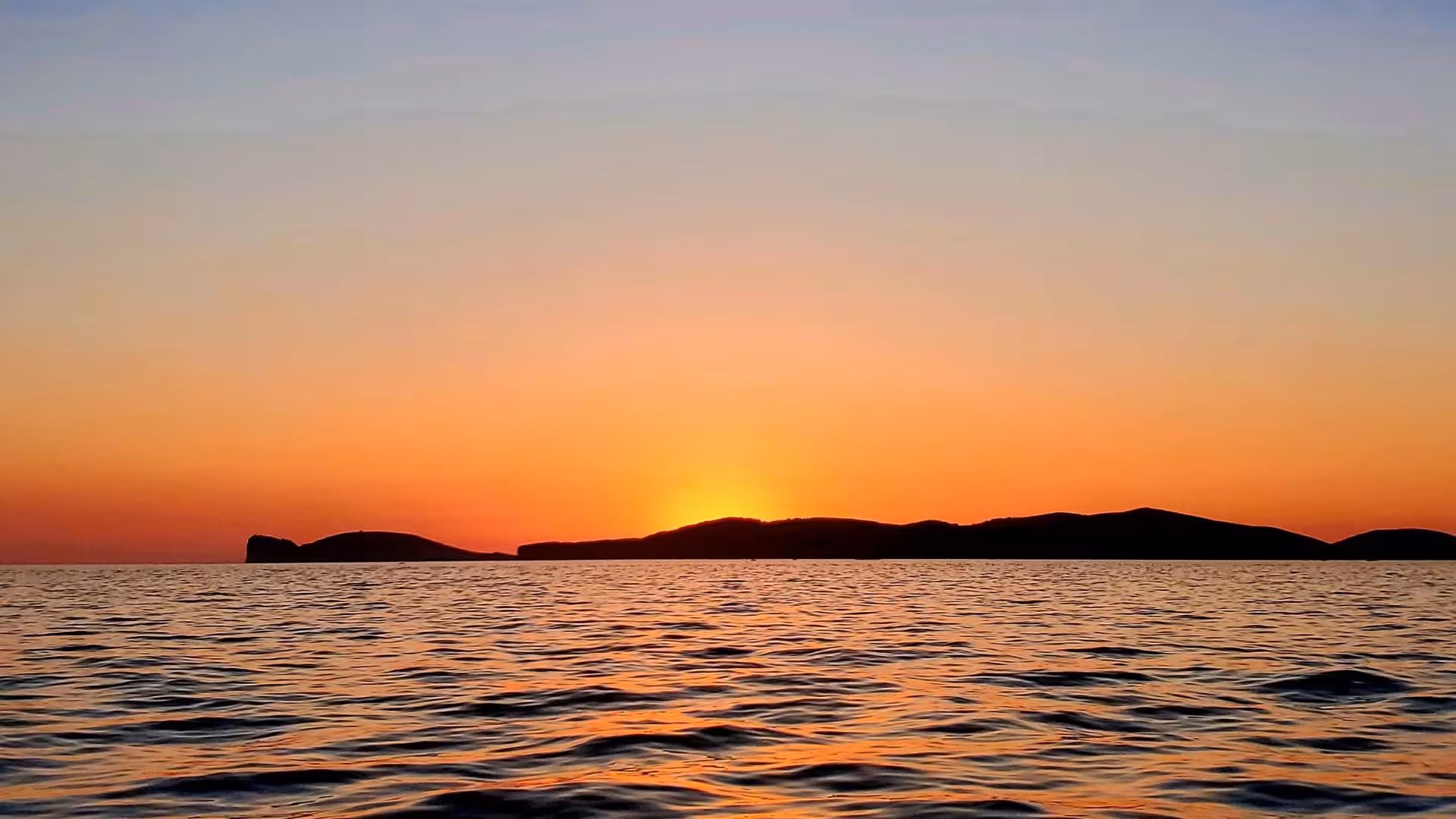 Vibrant sunset casting orange hues over the calm sea near Alghero, ideal for a scenic sailing tour.