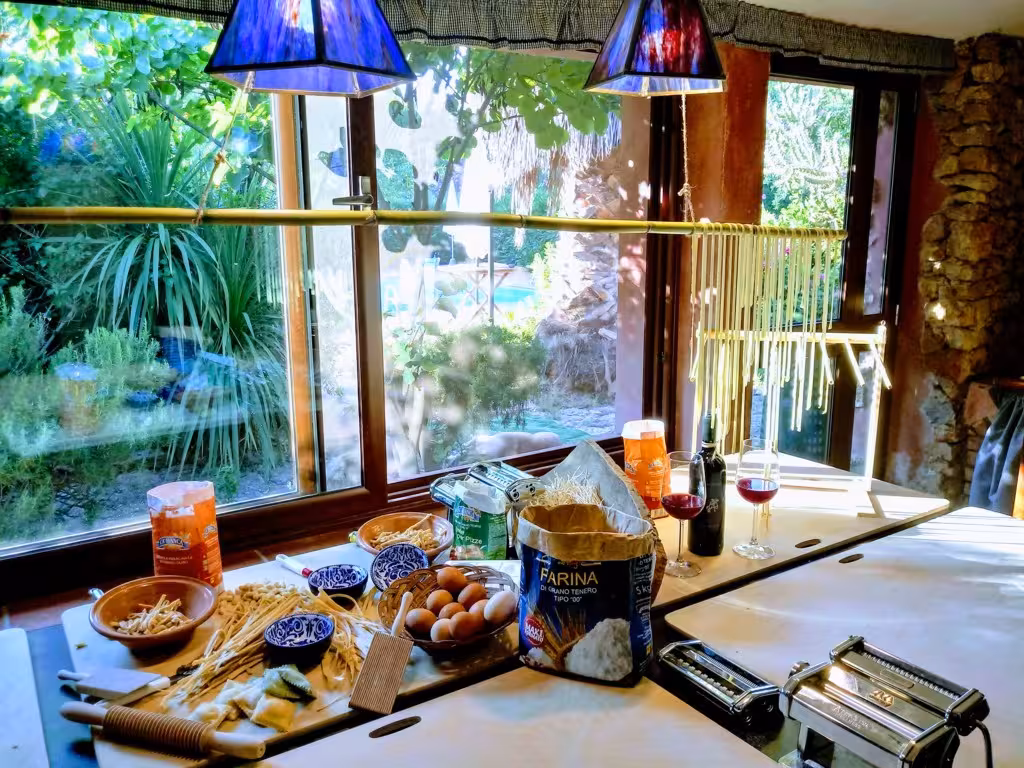 Scenic kitchen setup for traditional Italian cooking class in Olmedo, featuring fresh pasta and wine by a window.