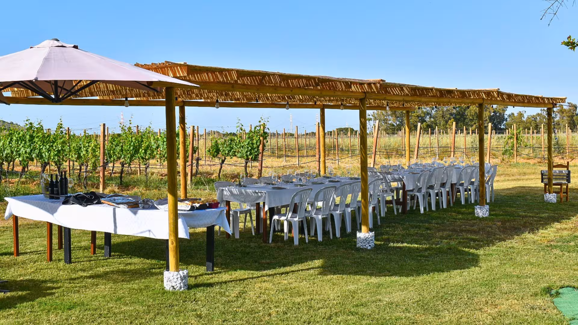 Outdoor dining setup with tables under a canopy in a lush Alghero vineyard, ideal for aperitif experiences.