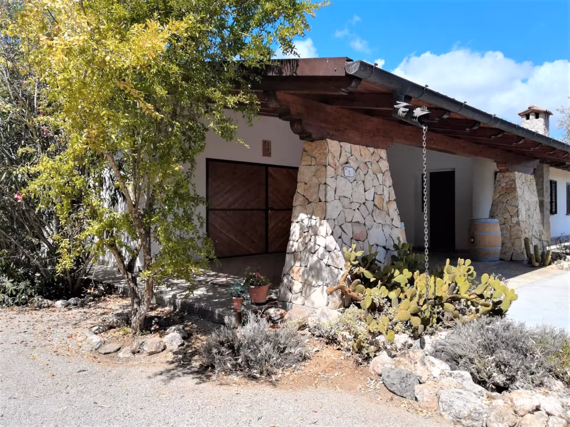 Rustic stone farmhouse entrance in Alghero surrounded by lush greenery, perfect for a vineyard dining tour.