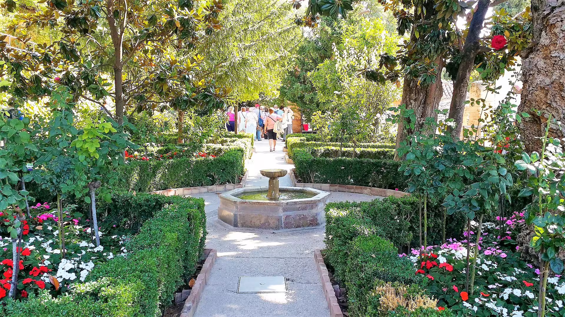 Group walking through Alhambra Generalife gardens with flowerbeds and fountain, guided tour in Granada