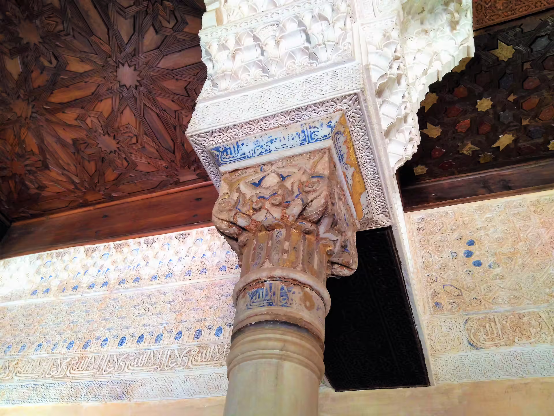Close-up of ornate Alhambra Nasrid column with Arabic calligraphy and carved stucco on guided group tour