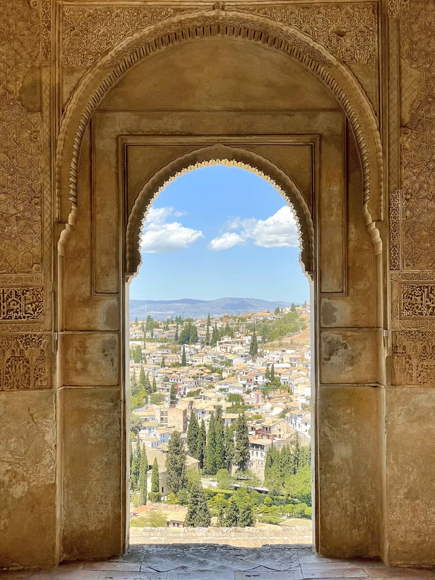 View through an ornate archway at the Alhambra, overlooking the scenic landscape and city of Granada, Spain.