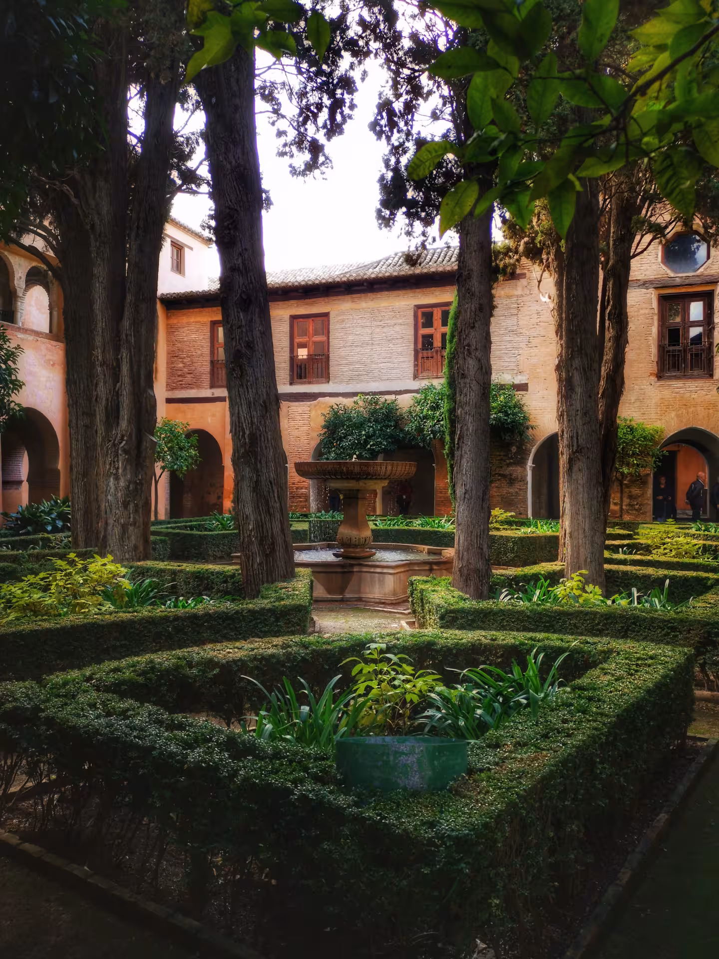 Lush courtyard garden with central fountain in the Alhambra, surrounded by historic Nasrid architecture.