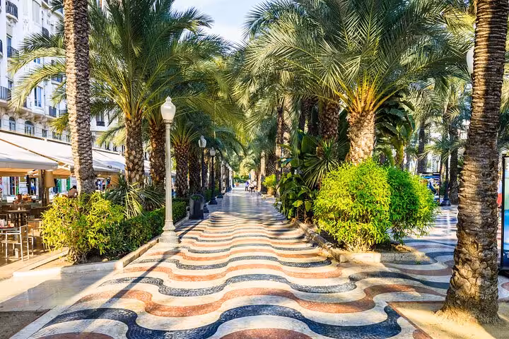 Scenic view of Alicante's Explanada de España lined with palm trees and vibrant mosaic tiles on a sunny day.