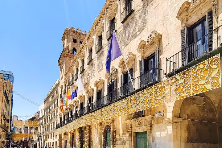 Historic building adorned with flags on a sunny day, highlighting Alicante's architectural charm.