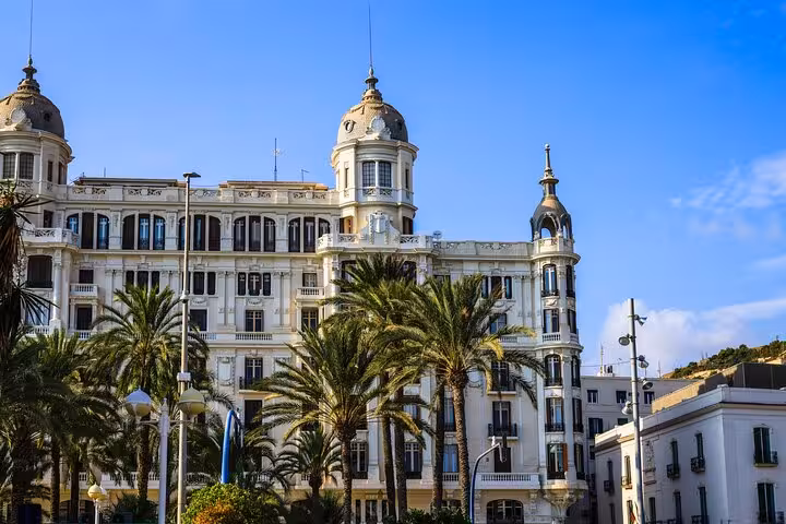 Majestic historic building with palm trees under a clear blue sky in Alicante, Spain, showcasing local architecture.