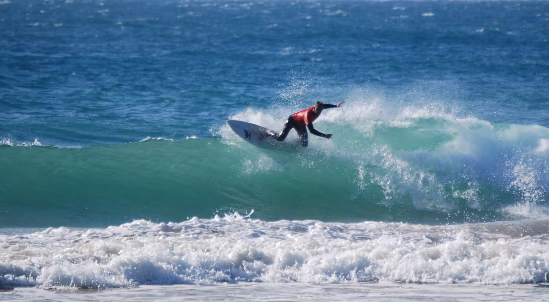 Expert surfer performing an aerial maneuver on a turquoise wave during a full-day surf tour in Aljezur