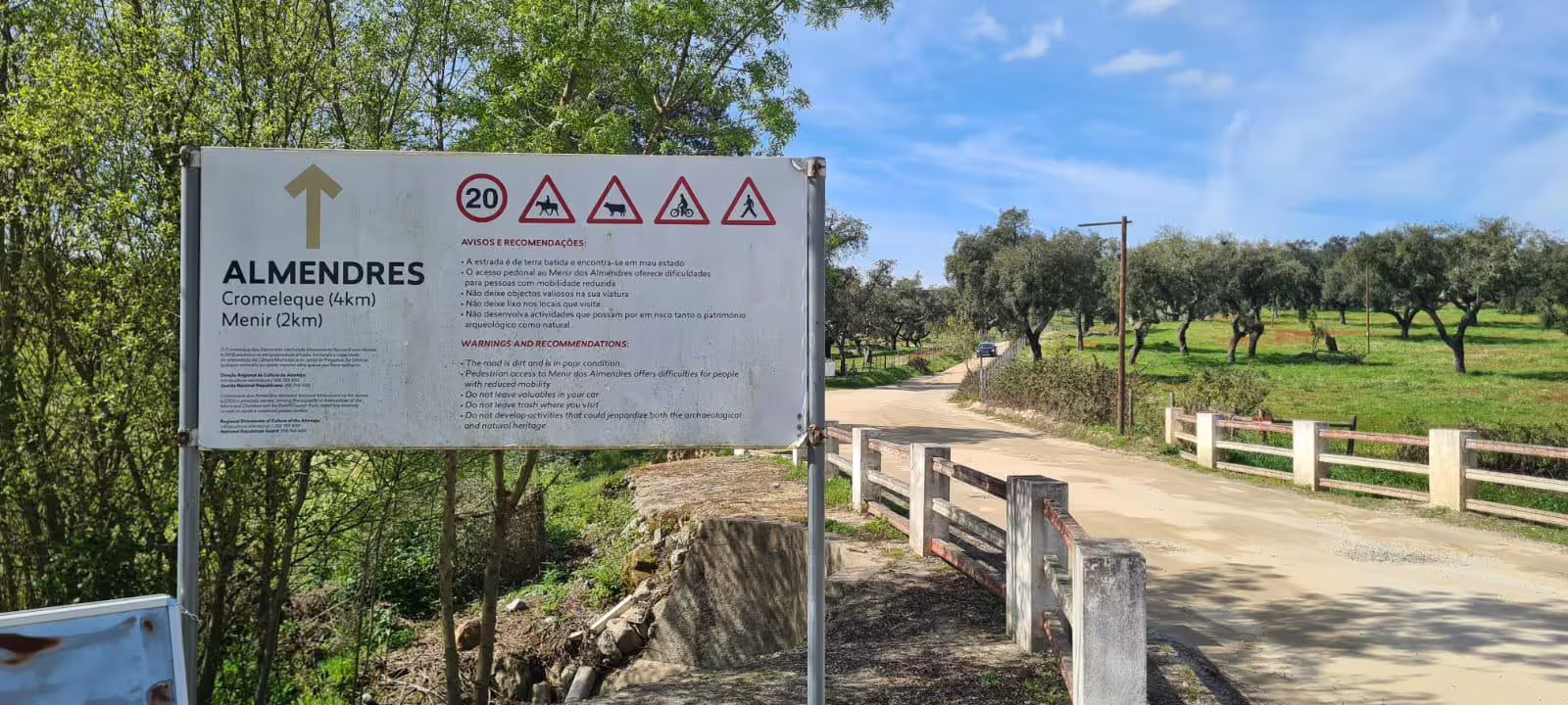 Directional sign for Almendres Cromlech and Menir with safety warnings, set against a scenic rural backdrop.