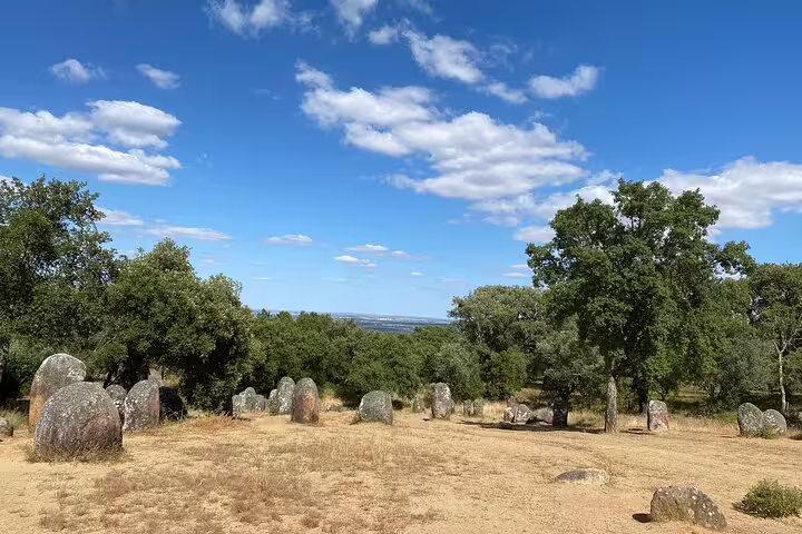 Discover the scenic Almendres Cromlech site with ancient stones under a vibrant sky on a tour from Lisbon to Évora.