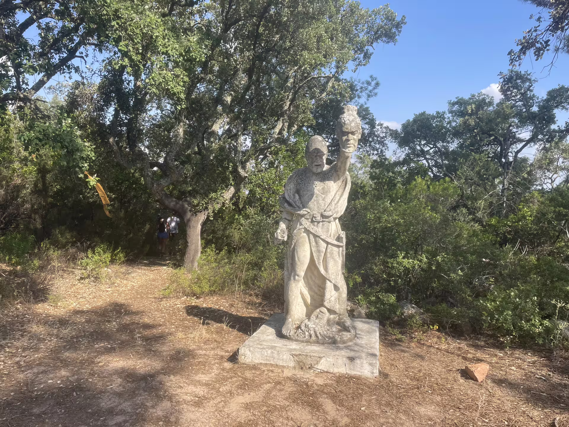 Ancient stone statue amidst lush greenery on the hiking trail to Almendres Cromlech in Évora, Portugal.