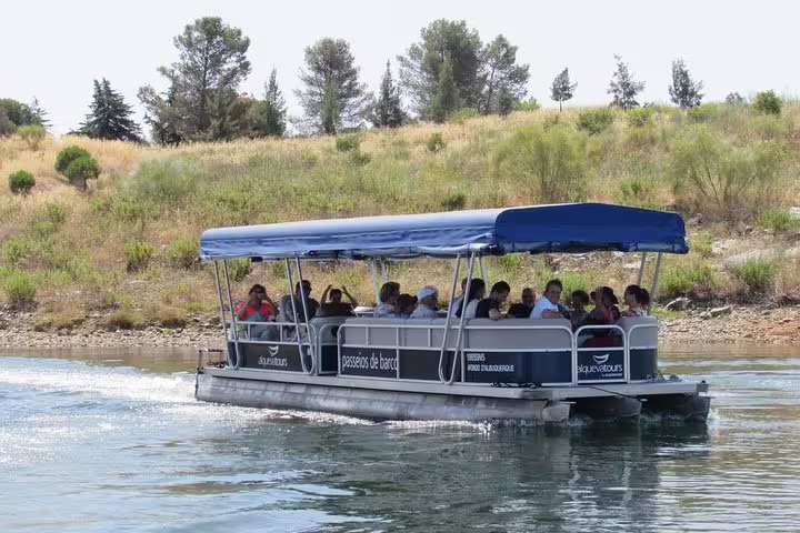 Tourists enjoy a scenic boat cruise on Alqueva Lake, surrounded by lush greenery and clear blue waters.