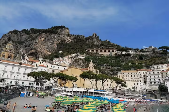 Vibrant Amalfi Coast beach scene with colorful umbrellas and historic hillside buildings on a sunny day.