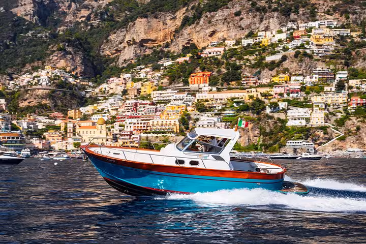 Charming boat cruising past colorful Positano cliffs on an exclusive Amalfi Coast experience.