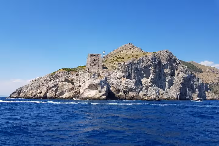 Historic coastal tower and lighthouse perched on rocky cliffs seen from an Amalfi Coast boat excursion.