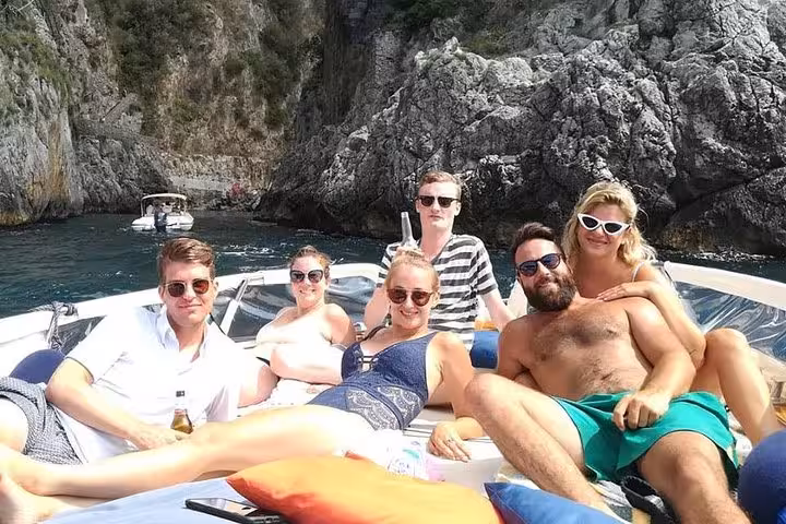 Relaxed tourists sunbathing on a boat amidst scenic cliffs during an Amalfi Coast tour from Sorrento.