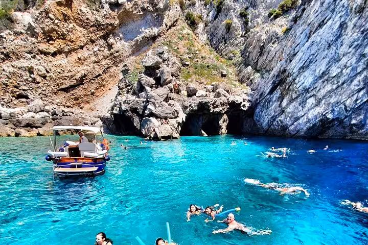 Visitors swimming in turquoise waters near rocky cliffs on an Amalfi Coast boat tour from Naples.