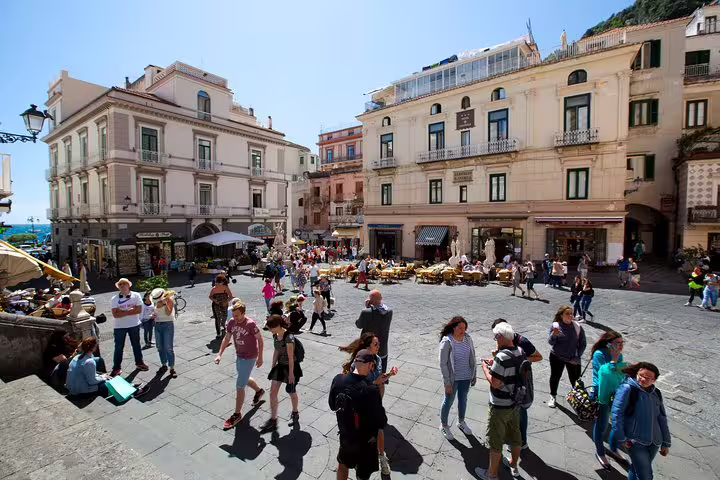 Tourists exploring the vibrant central square of Amalfi with historic buildings and bustling cafes.