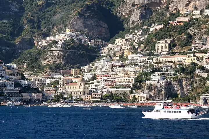 Cruise excursion boat sailing past colorful cliffside houses of Positano village on Italy’s scenic Amalfi Coast