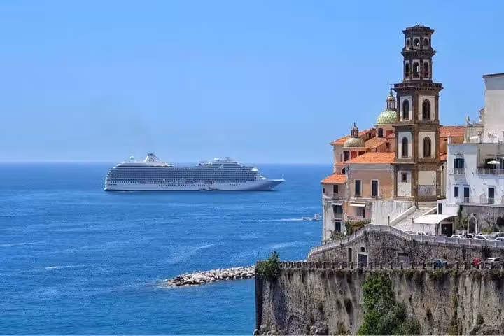 Cruise ship sailing past the picturesque Amalfi coast with historic buildings perched on the cliffside.