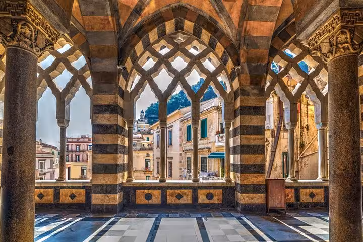 Intricate gothic arches and columns framing a view of Amalfi town buildings on the Amalfi Coast.