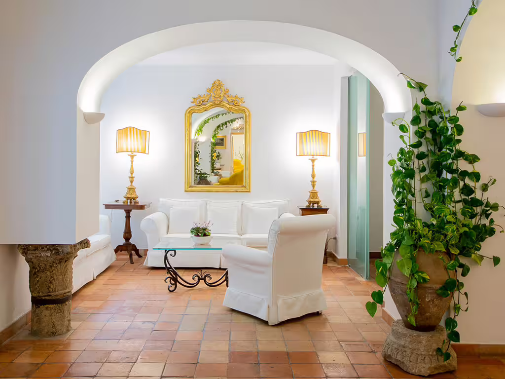 Cozy white sitting area in Amalfi Coast hotel with archway, gold mirror, indoor plants and romantic ambient lighting