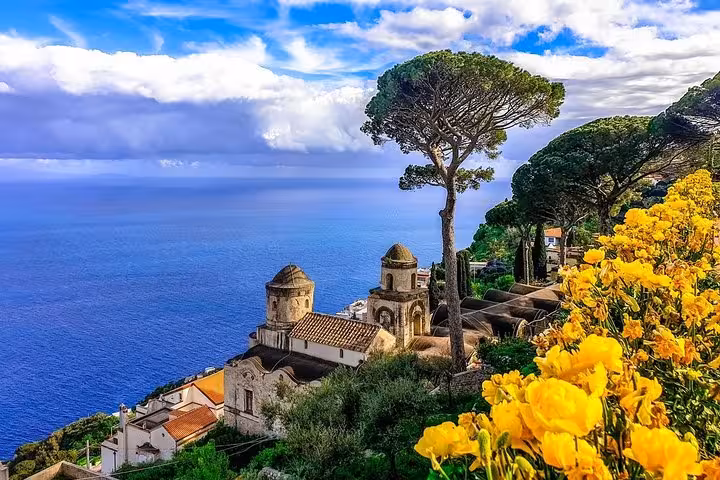 Breathtaking view of Amalfi Coast's coastline with historic architecture and vibrant flowers under a blue sky.