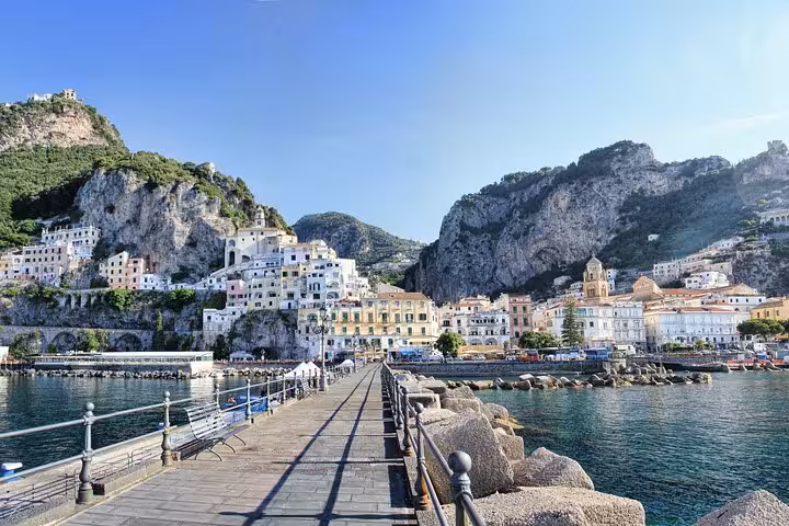 Picturesque pier leading to the scenic town of Amalfi, nestled between rugged cliffs and the calm blue sea.