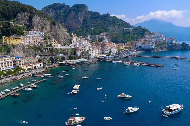 Aerial view of Amalfi Coast's vibrant harbor with boats, historic buildings, and lush hillsides, ideal for a tour from Sorrento.