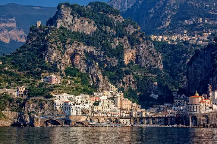 Picturesque view of Amalfi Coast's rugged cliffs and charming coastal village with pastel buildings and lush greenery.